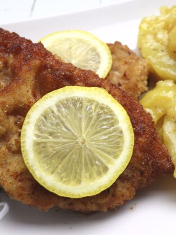 German schnitzel with potato salad garnished with lemon slice and parsley.