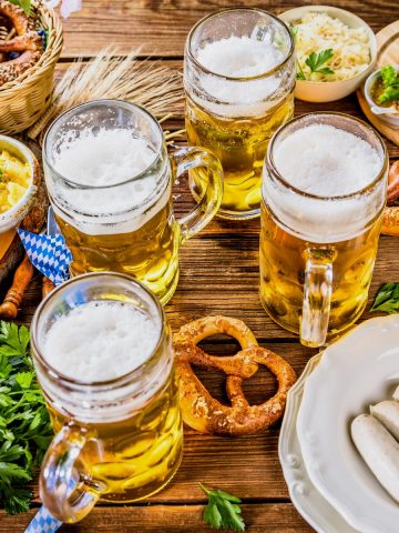 Bavarian white sausages, pretzels, German beer, German potato salad, and sweet mustard on a wooden table in Oktoberfest decoration.