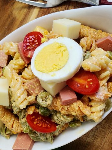 German nudelsalat in a white bowl, garnished with a slice of egg, on a wooden board.