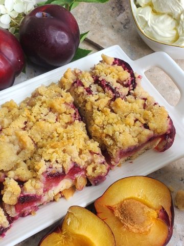Slices of German Pflaumekuchen with plum, whipped cream and coffee cup in the background.