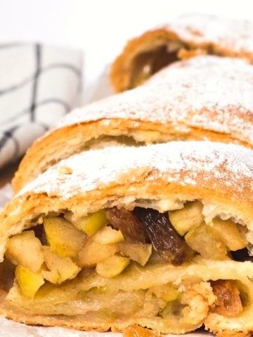 German apple strudel sprinkled with powdered sugar on a white plate.