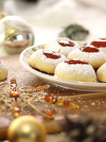 Engelsaugen filled with raspberry jam aka German thumbprint cookies on a Christmas plate on a wooden board in Christmas decoration.