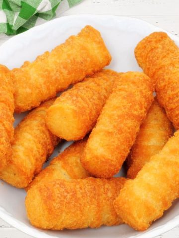 Kroketten on a white plate with a green-white napkin in the left corner on a white wooden table.