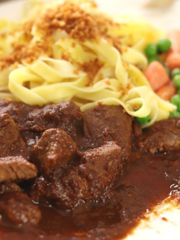 Traditional Gulasch on a plate with noodles and veggies.