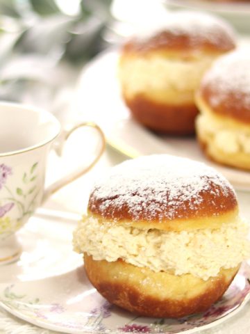 Bavarian cream donuts on a plate with coffee cup on the left side. More Bavarian cream donuts on a platter in the background.