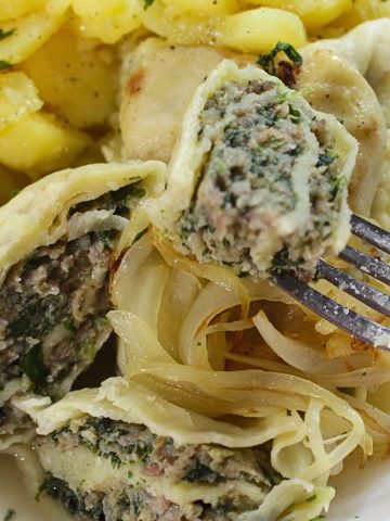 Maultaschen with caramelized onions and potato salad on a white plate.