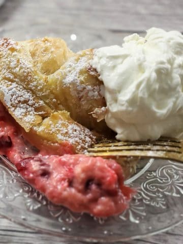 Slice of cherry strudel on a glass plate with fork.